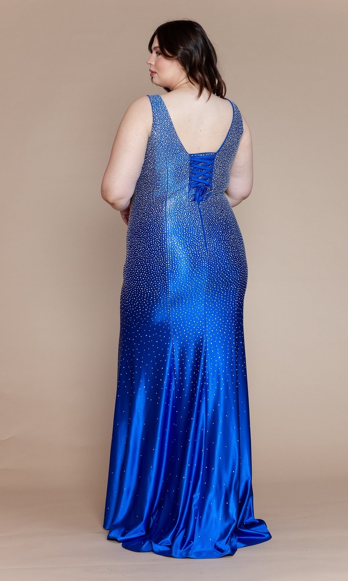 A woman stands facing away in the Spandex Long Beaded Plus-Size Prom Dress W1130—a sleeveless, floor-length blue gown with a gradient design and sparkling embellishments—set against a plain beige background.